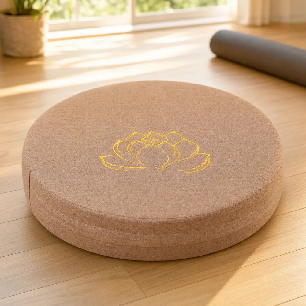 Low round meditation cushion set up on a wooden floor beside a folded blanket, ready for a sitting session
