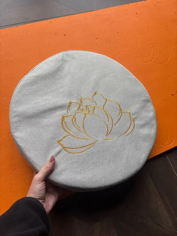 Buyer photo of a white meditation cushion held above an orange yoga mat