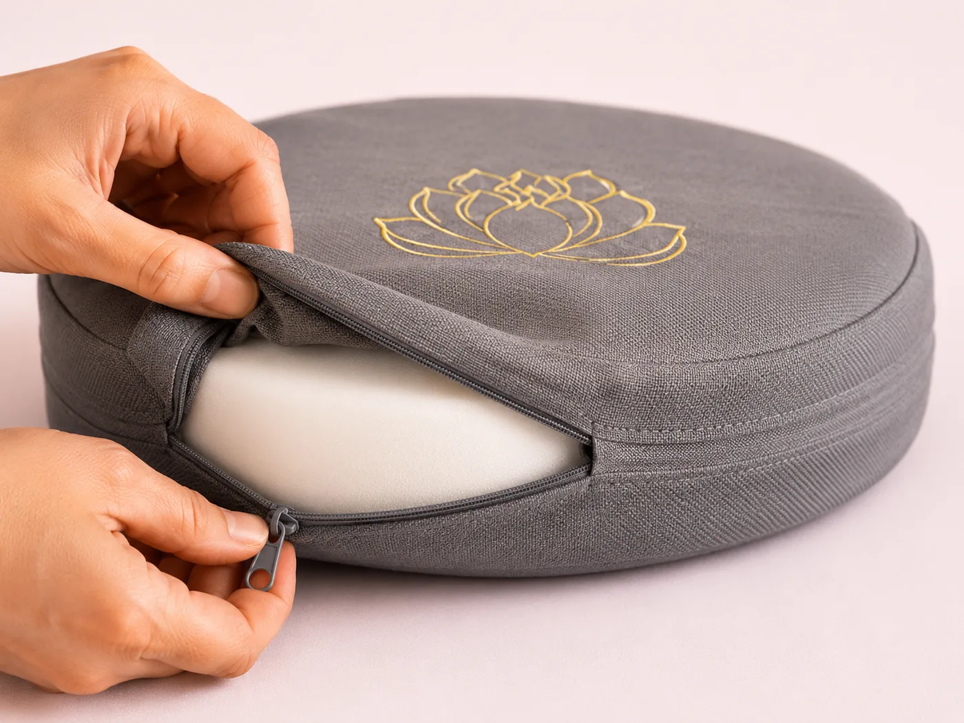 A hand unzipping the removable linen cover from a gray StillSeat meditation cushion